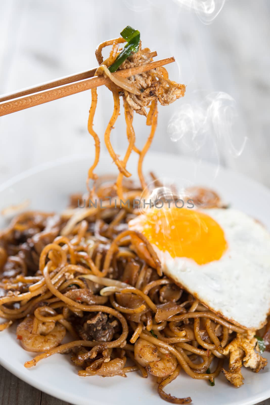 Stir fried char kway teow with prawns and chopstick over wooden background. 