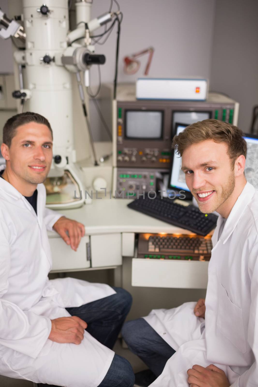 Biochemistry student using large microscope and computer by Wavebreakmedia