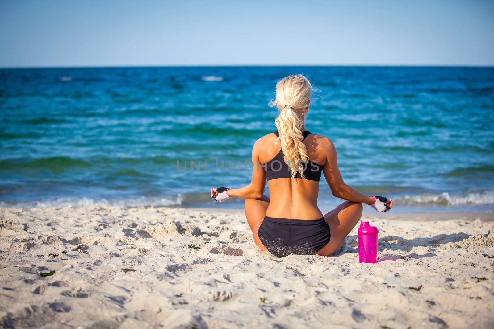 beautiful young woman sitting in yoga pose at the beach 
