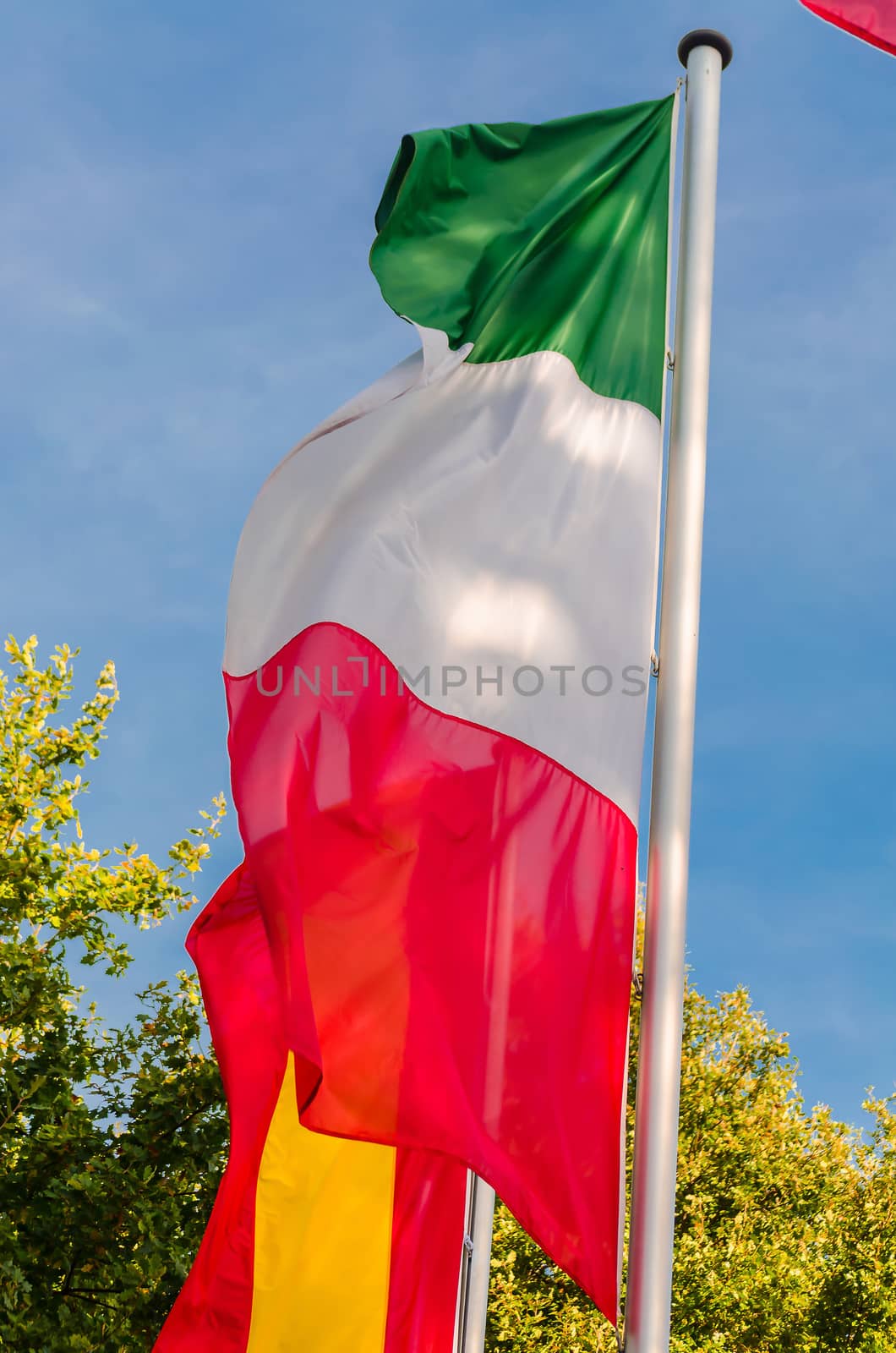 Italian flag on a flag pole waving in the wind against blue sky