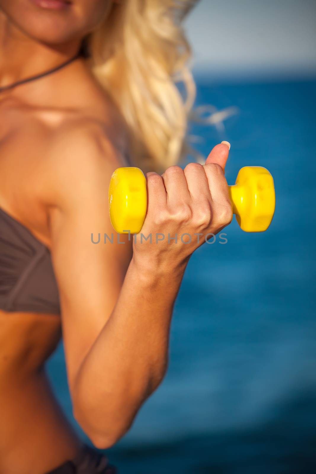 Sweaty fitness woman working out with dumbbells in summer on beach