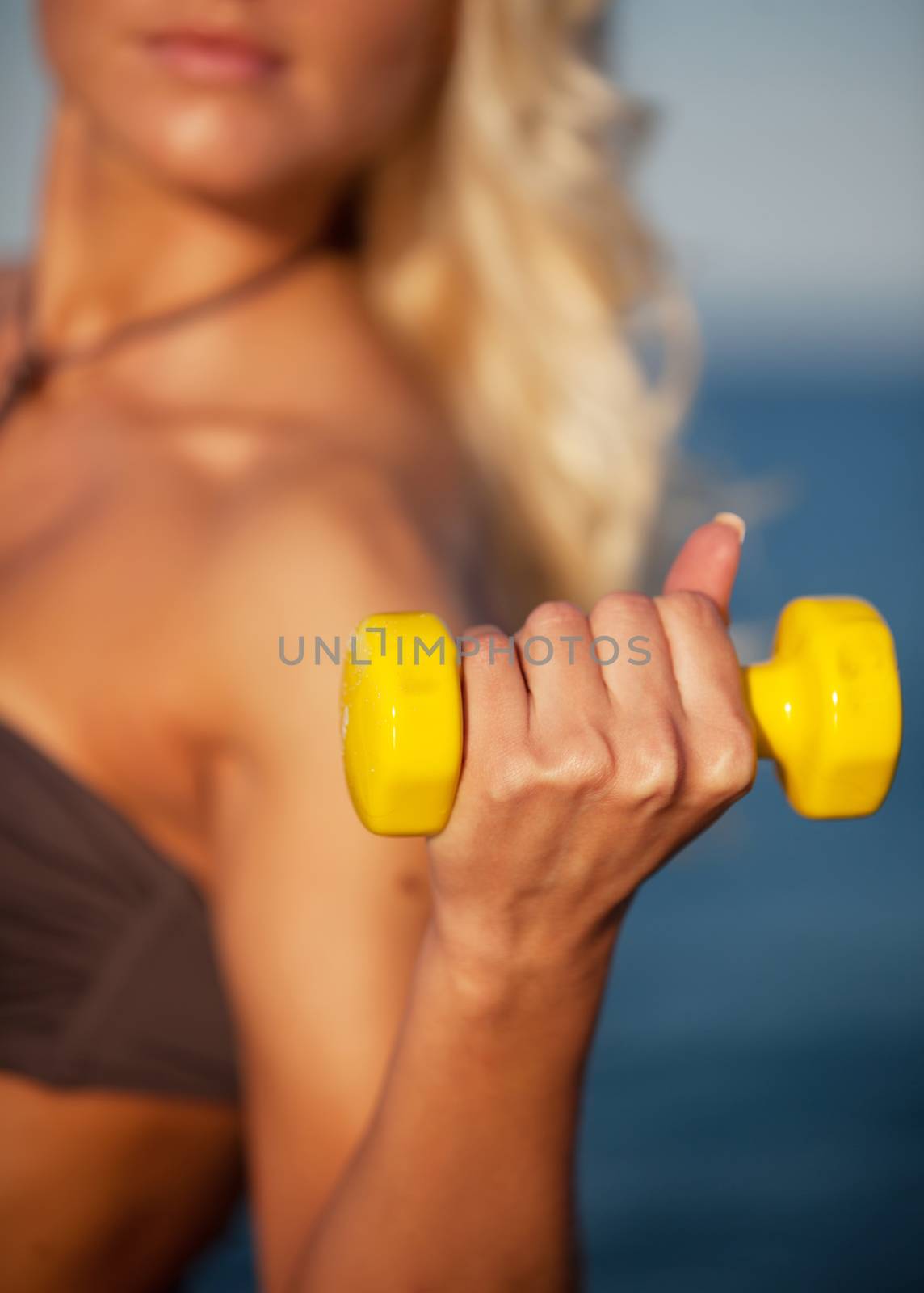Sweaty fitness woman working out with dumbbells in summer on beach