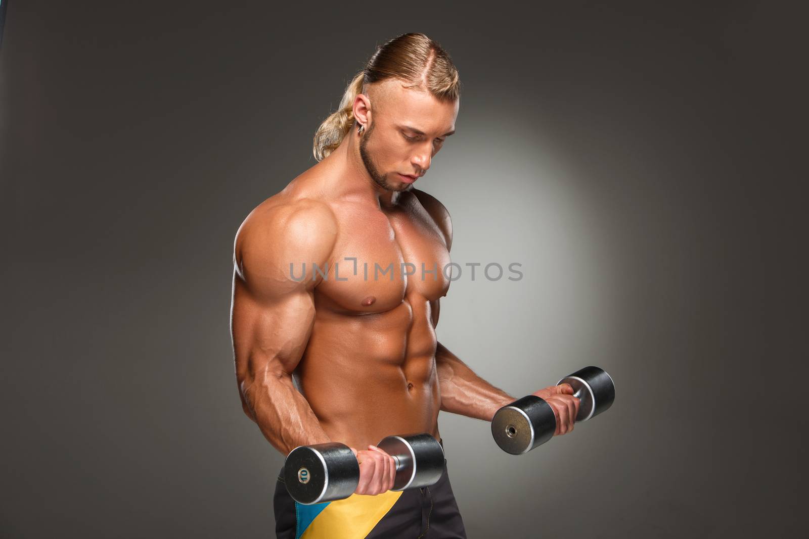 Attractive male body builder with dumbbells on gray background.