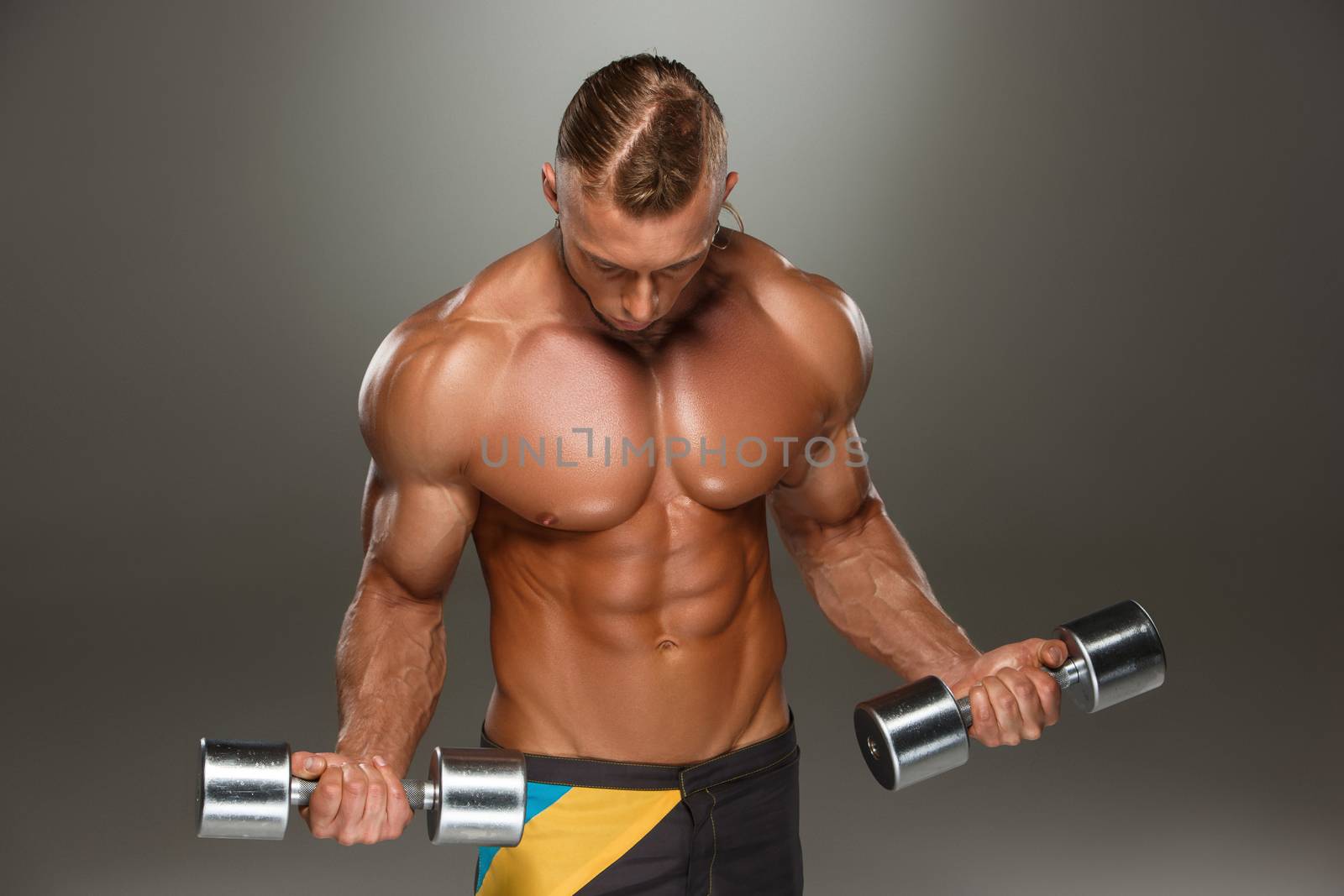 Attractive male body builder with dumbbells on gray background.