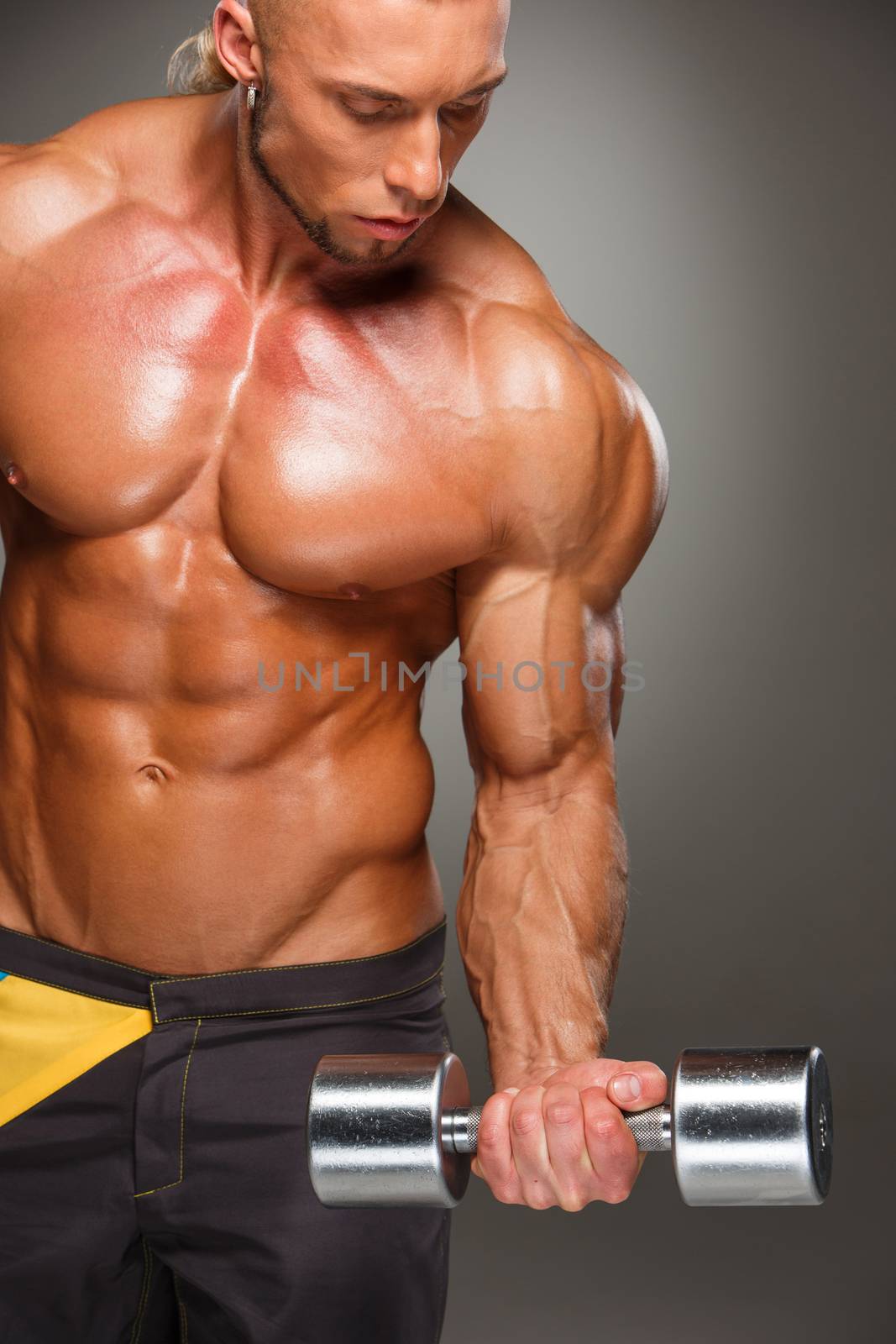 Attractive male body builder with dumbbell on gray background.
