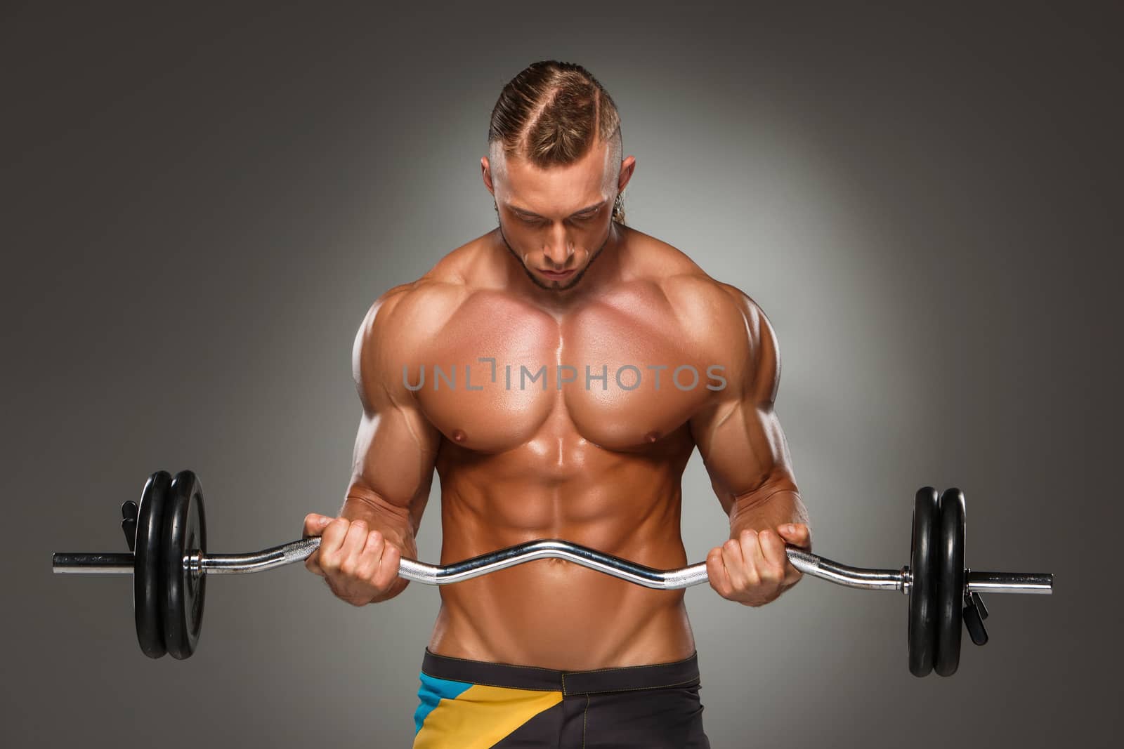 Portrait of super fit muscular young man working out in gym with barbell on gray background 