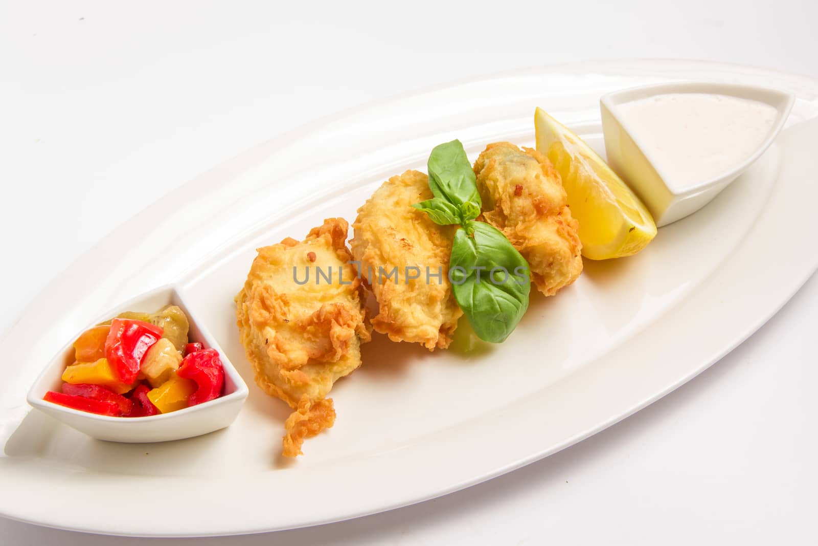 Fried fish in batter with sauce, lemon and vegetables. On white background