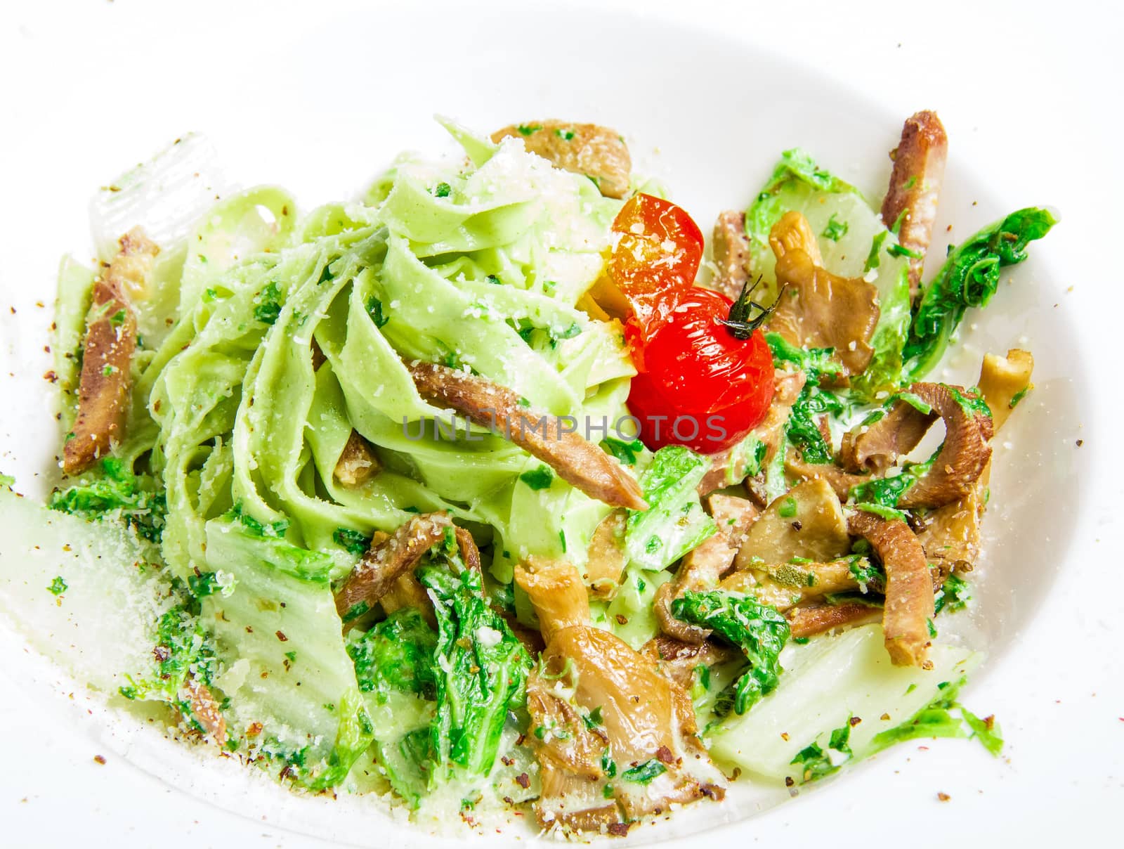 green pasta with meat, grated cheese, tomatoes, cabbage and gravy on a white plate