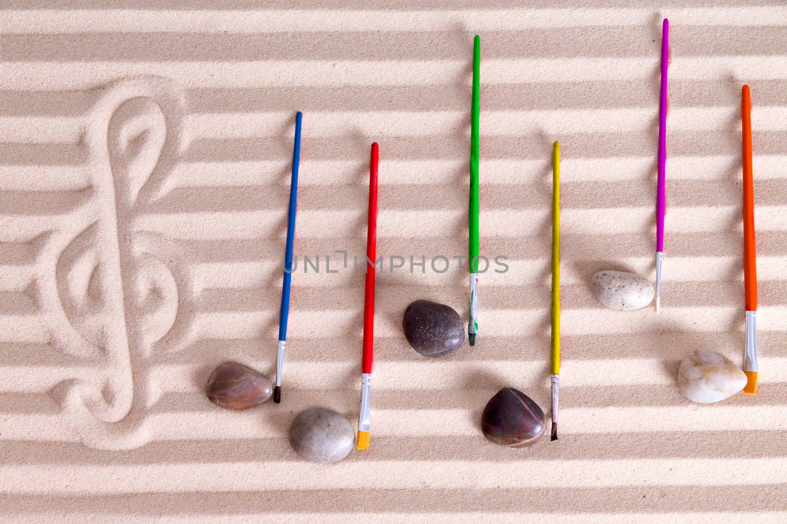 Music at the seaside concept with an artistic arrangement of music notes formed from pebbles and colorful paintbrushes on a background score composed of alternating lines of golden sand