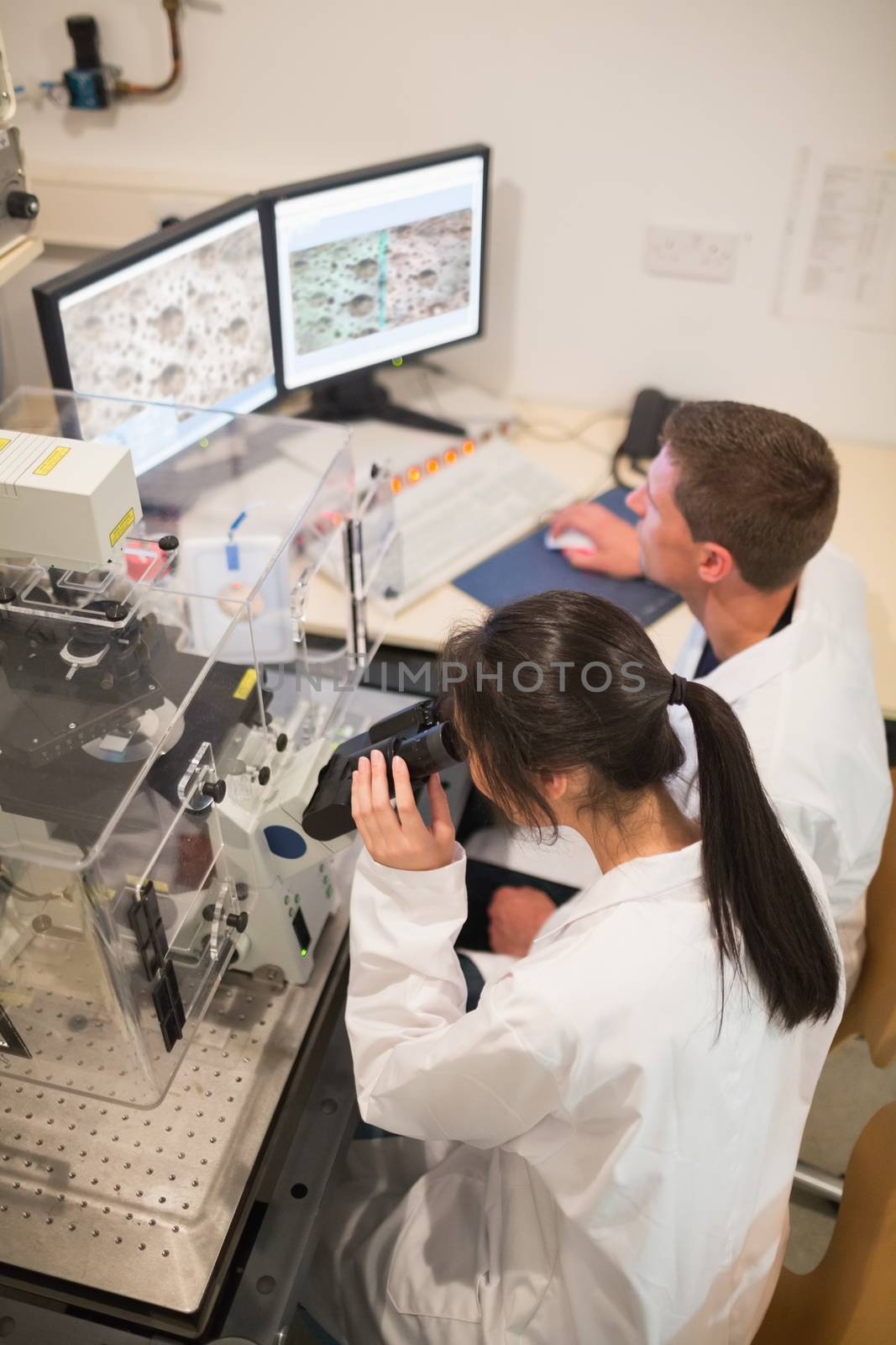 Biochemistry students using large microscope and computer by Wavebreakmedia