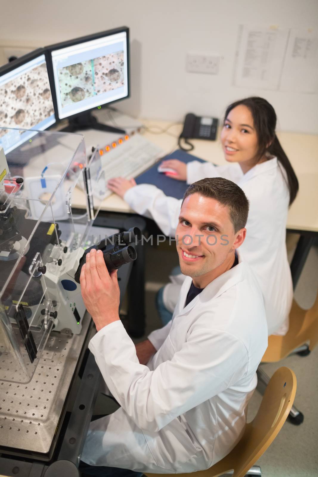 Biochemistry students using large microscope and computer by Wavebreakmedia