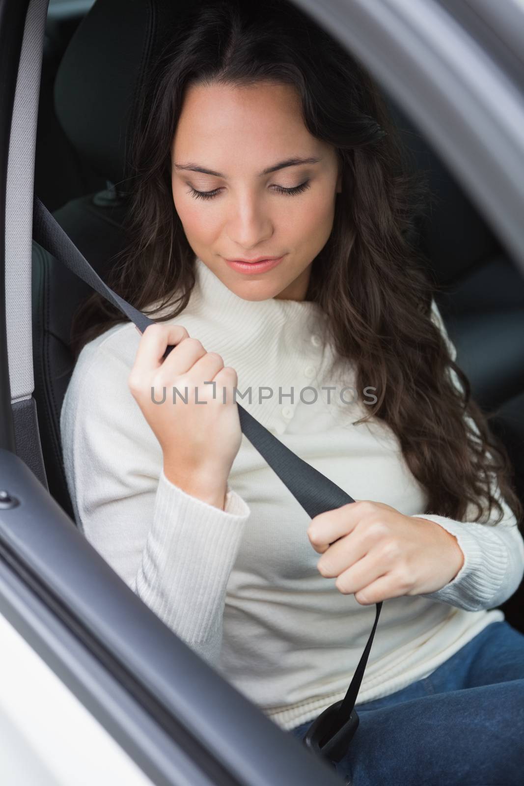 Woman putting on her seat belt in her car