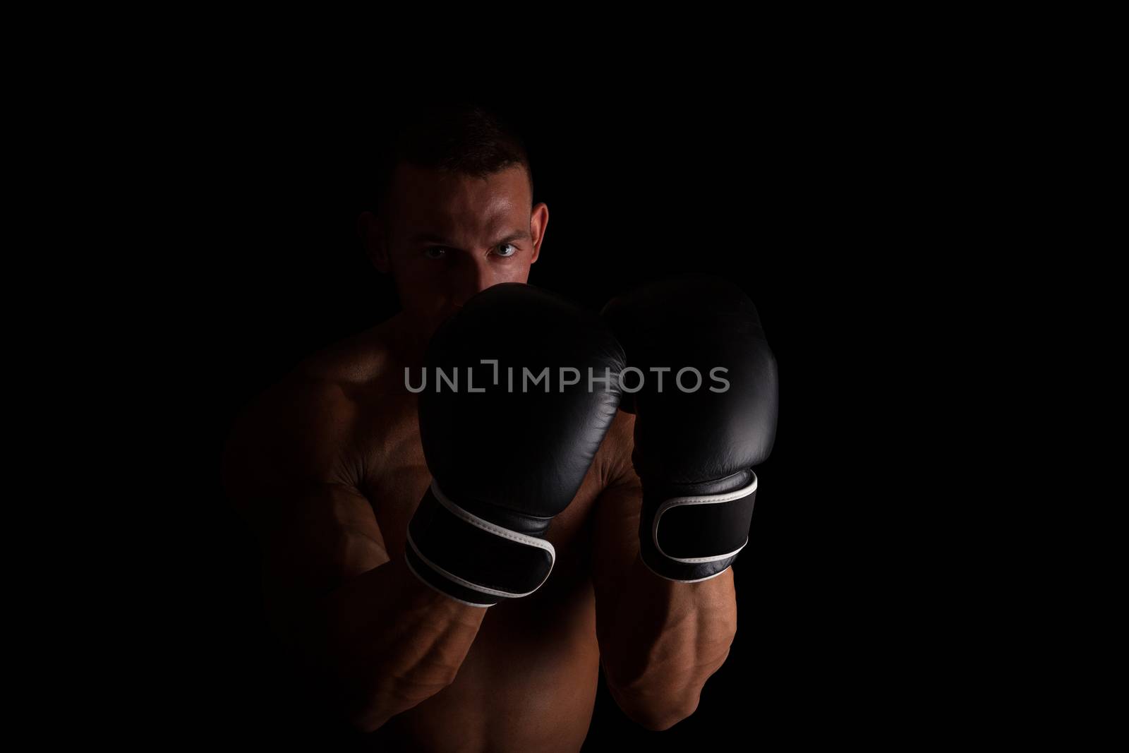 Boxer. Young sexy muscular shirtless man with boxing gloves looking into camera isolated on black background. Sport and fitness.  