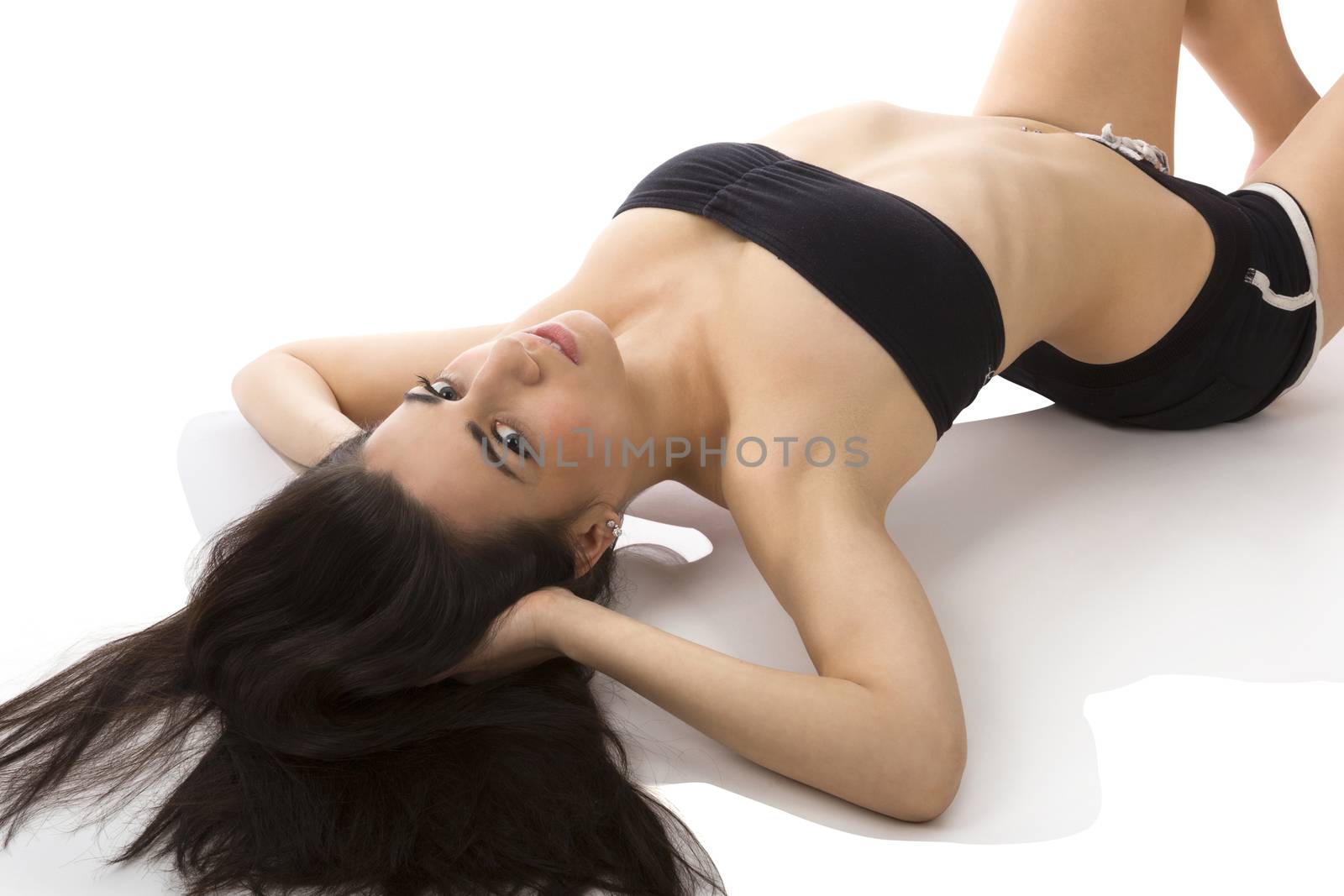 Sexy brunette in hot pants and sports bra stretching on white background. Hot, sexy and fit. 
