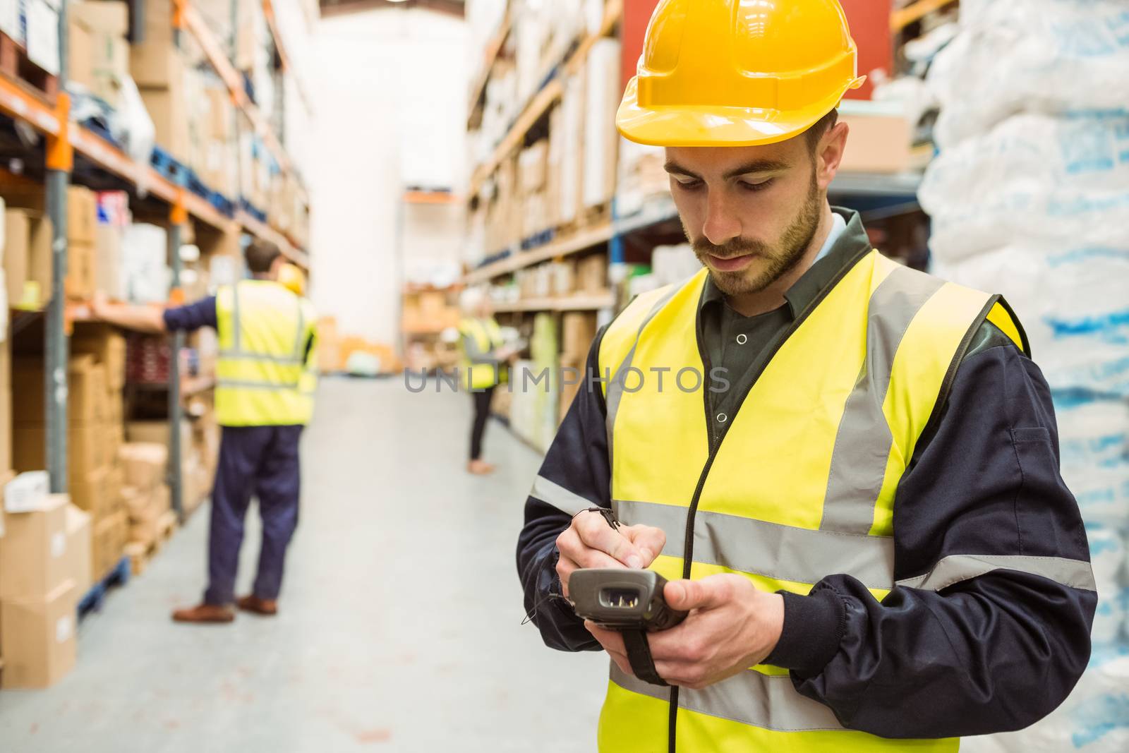 Focused worker wearing yellow vest using handheld in a large warehouse