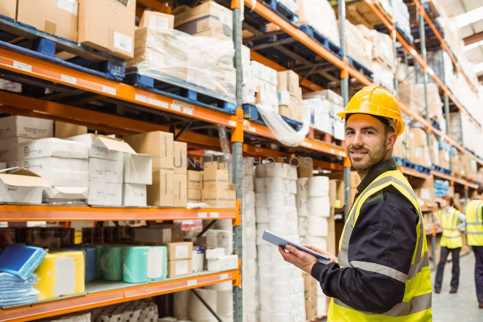 Smiling warehouse manager holding clipboard in a large warehouse