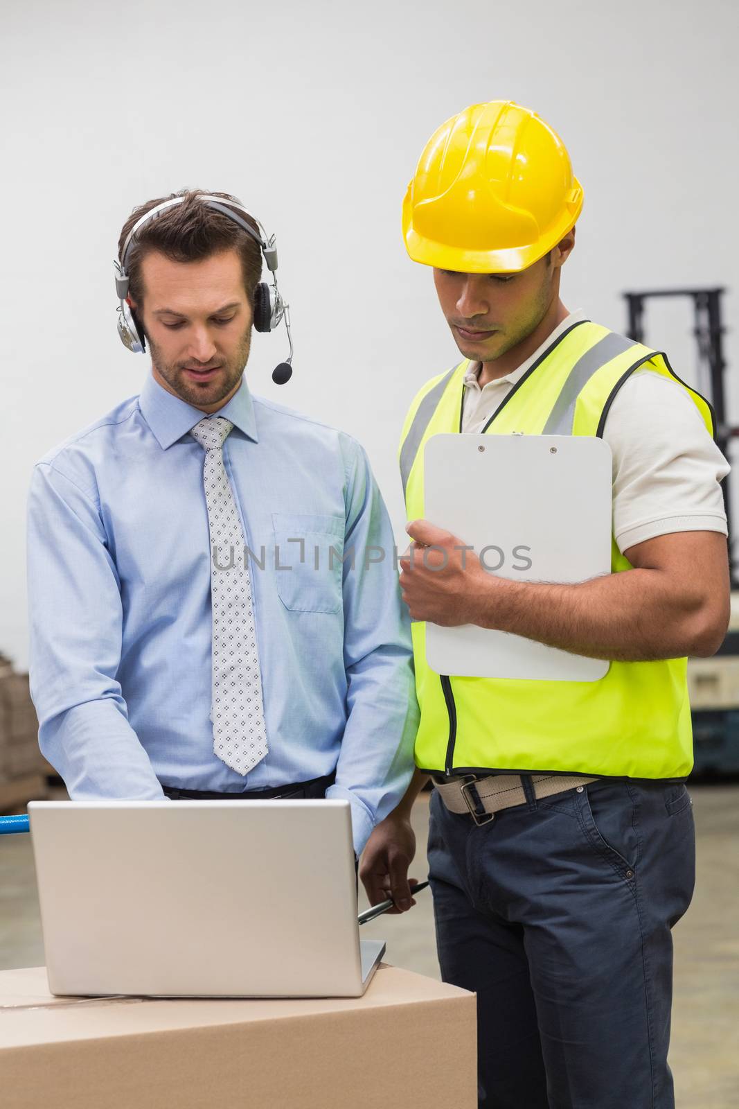 Warehouse worker and manager looking at laptop in a large warehouse