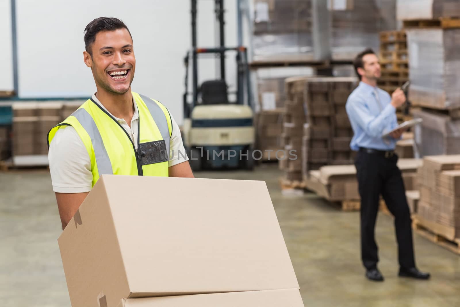 Smiling warehouse worker moving boxes on trolley in a large warehouse