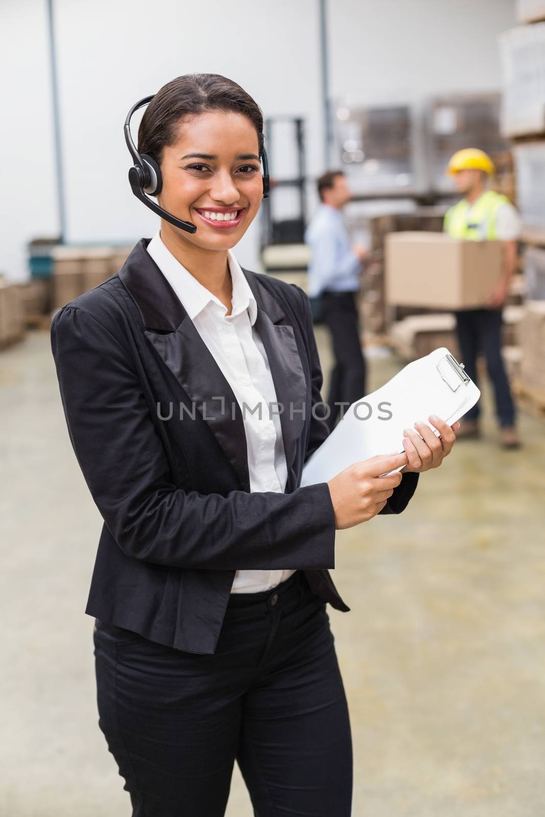 Warehouse manager wearing headset holding clipboard by Wavebreakmedia