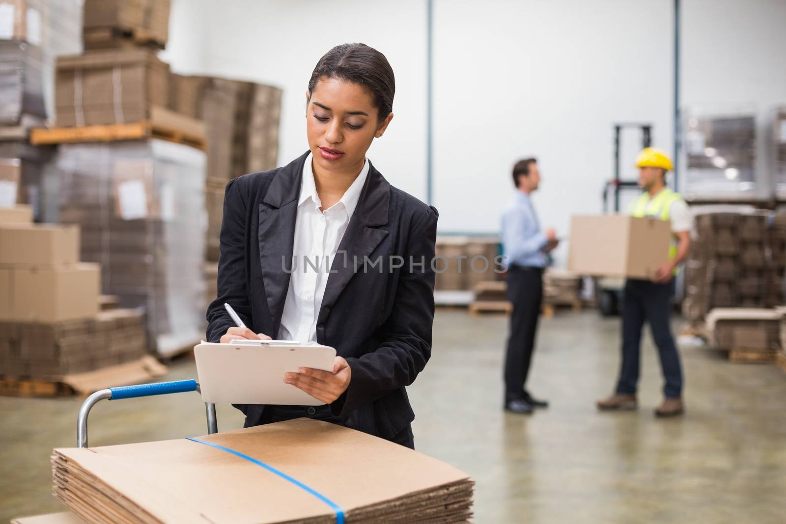 Pretty warehouse manager writing on clipboard in a large warehouse