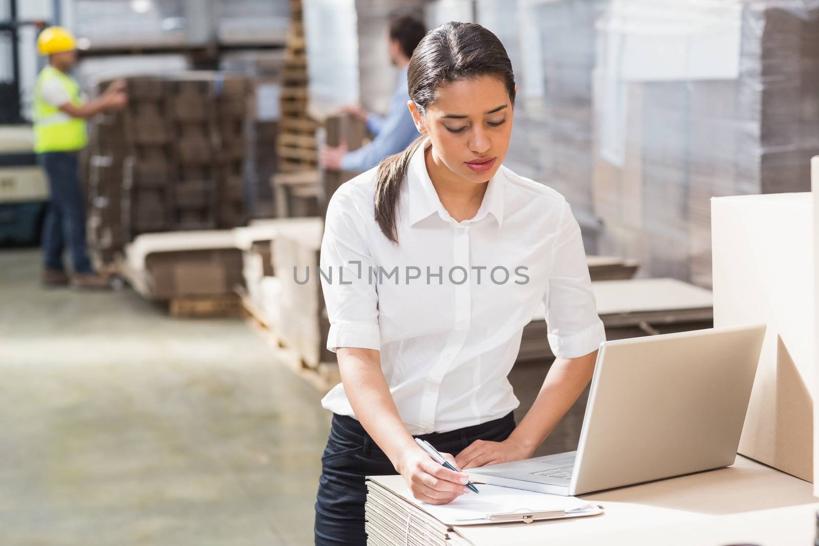 Warehouse manager using laptop and clipboard in a large warehouse