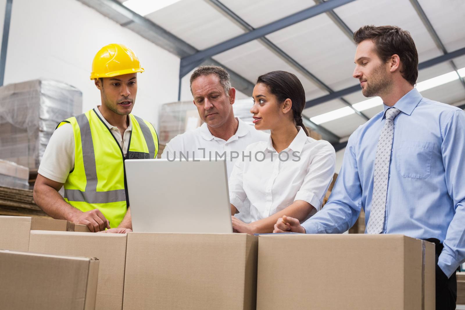 Warehouse managers and worker looking at laptop in a large warehouse