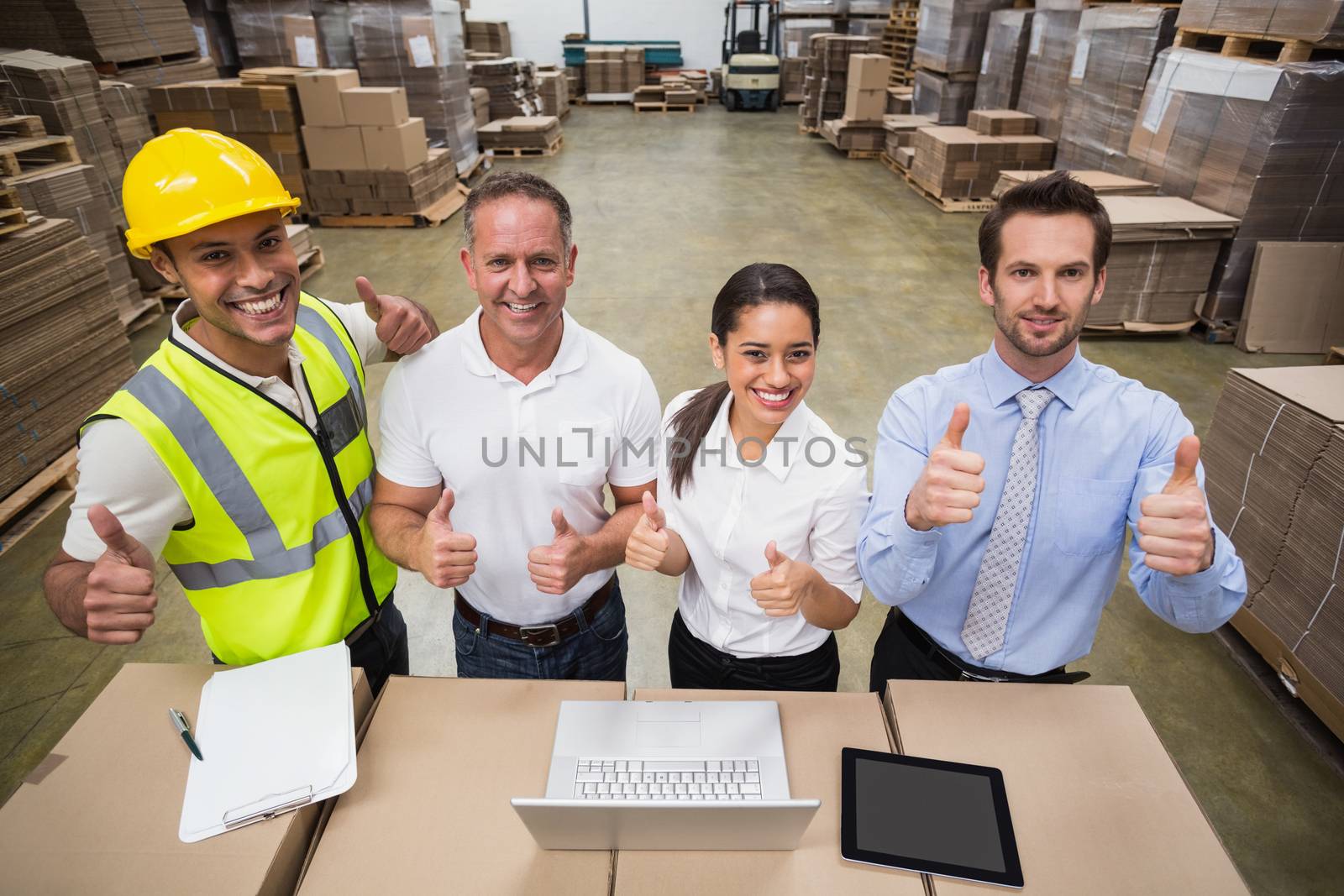 Warehouse team smiling at camera showing thumbs up in a large warehouse