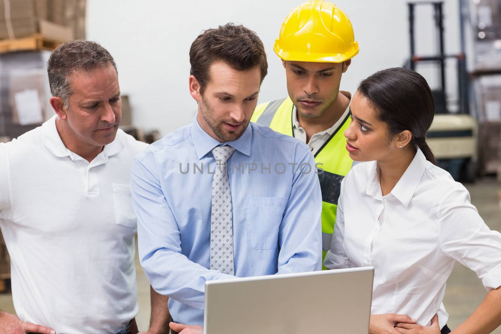 Warehouse managers and worker looking at laptop in a large warehouse