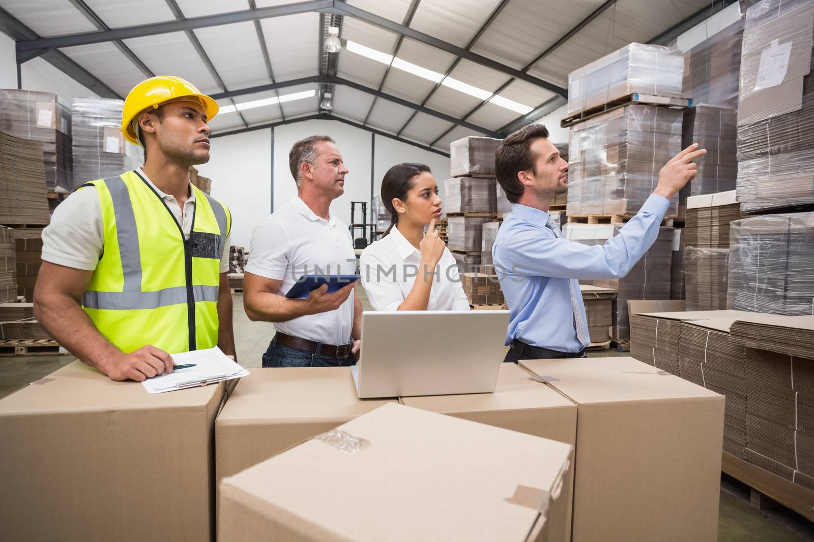 Warehouse manager pointing something to his colleagues in a large warehouse