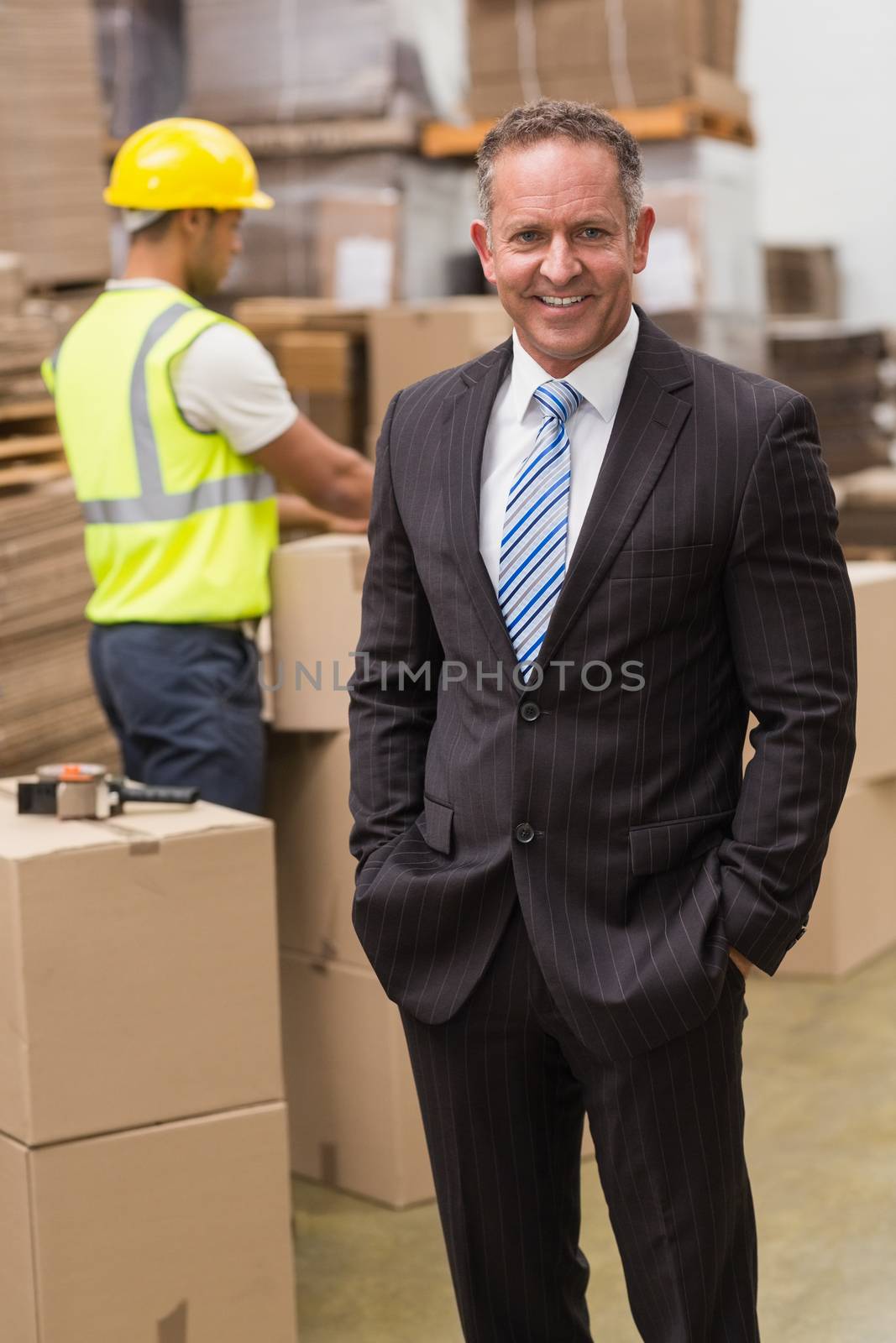 Smiling boss standing with hands in pockets in a large warehouse