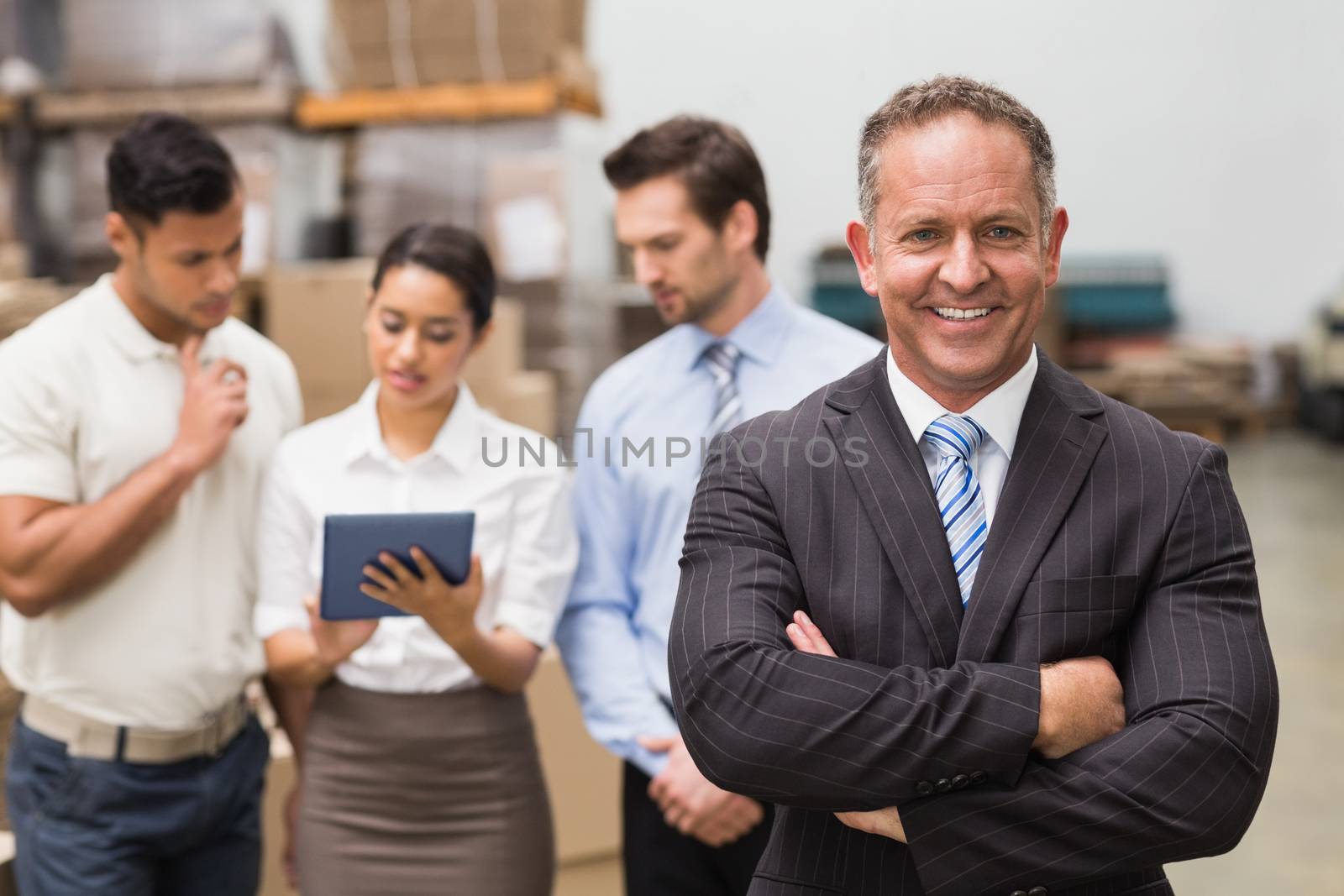 Boss standing with arms crossed in front of his employees in a large warehouse