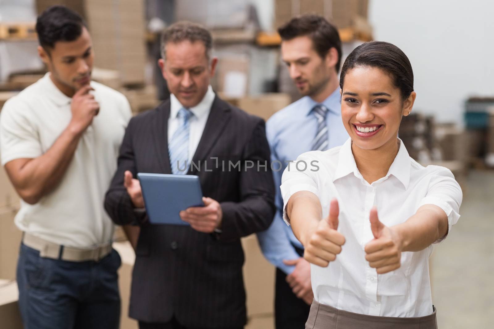 Manager showing thumbs up in front of her colleagues in a large warehouse