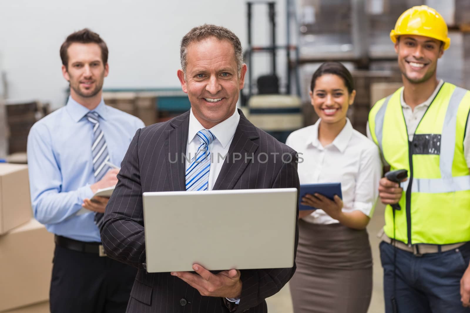 Smiling boss using laptop in front of his employees by Wavebreakmedia