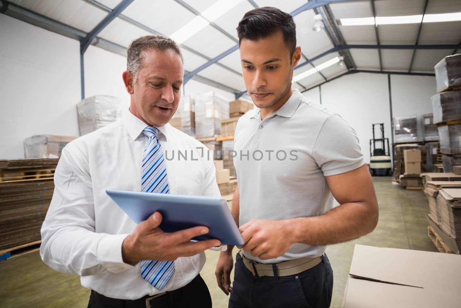 Warehouse manager using tablet pc with colleague in a large warehouse