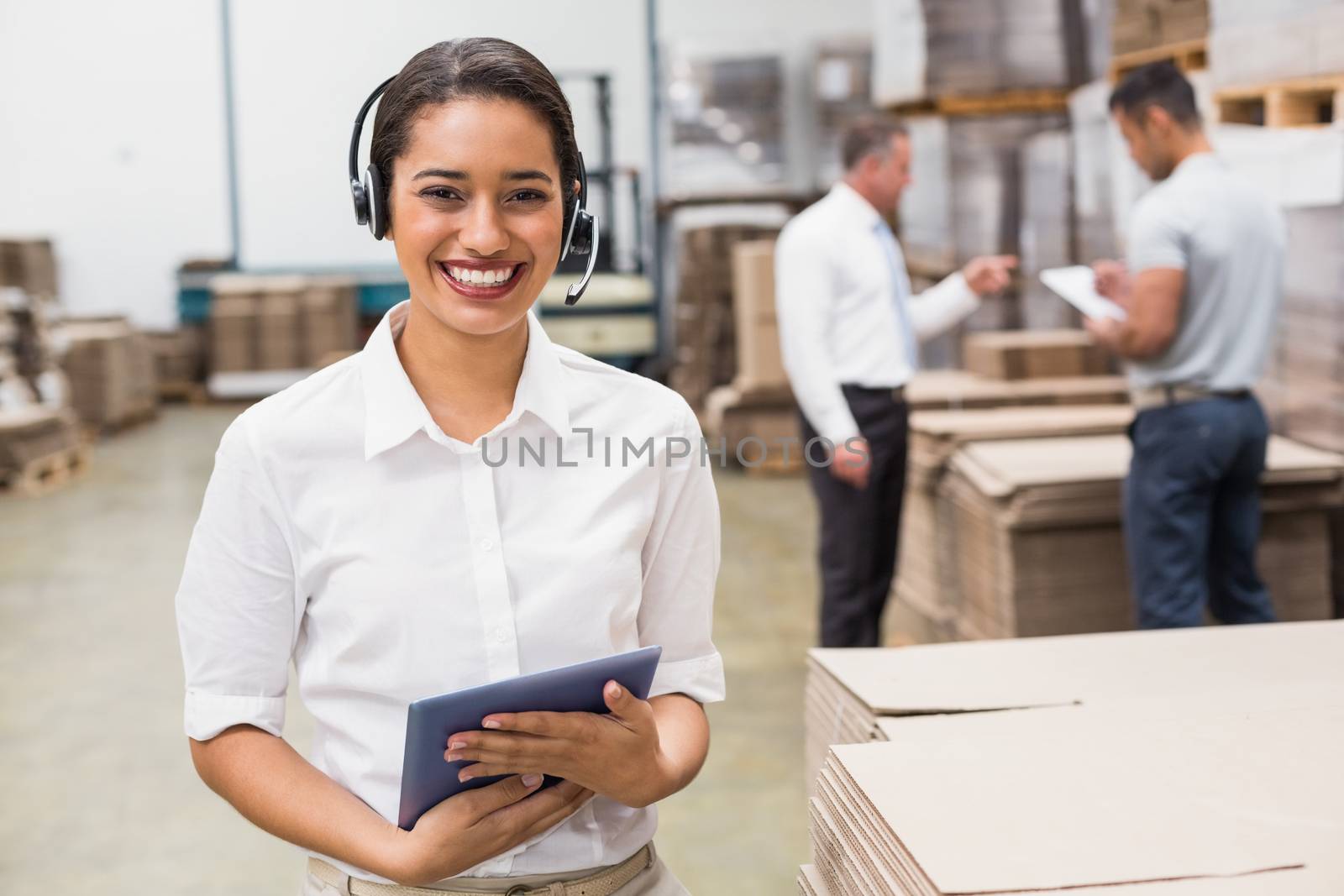 Warehouse manager wearing headset holding clipboard in a large warehouse