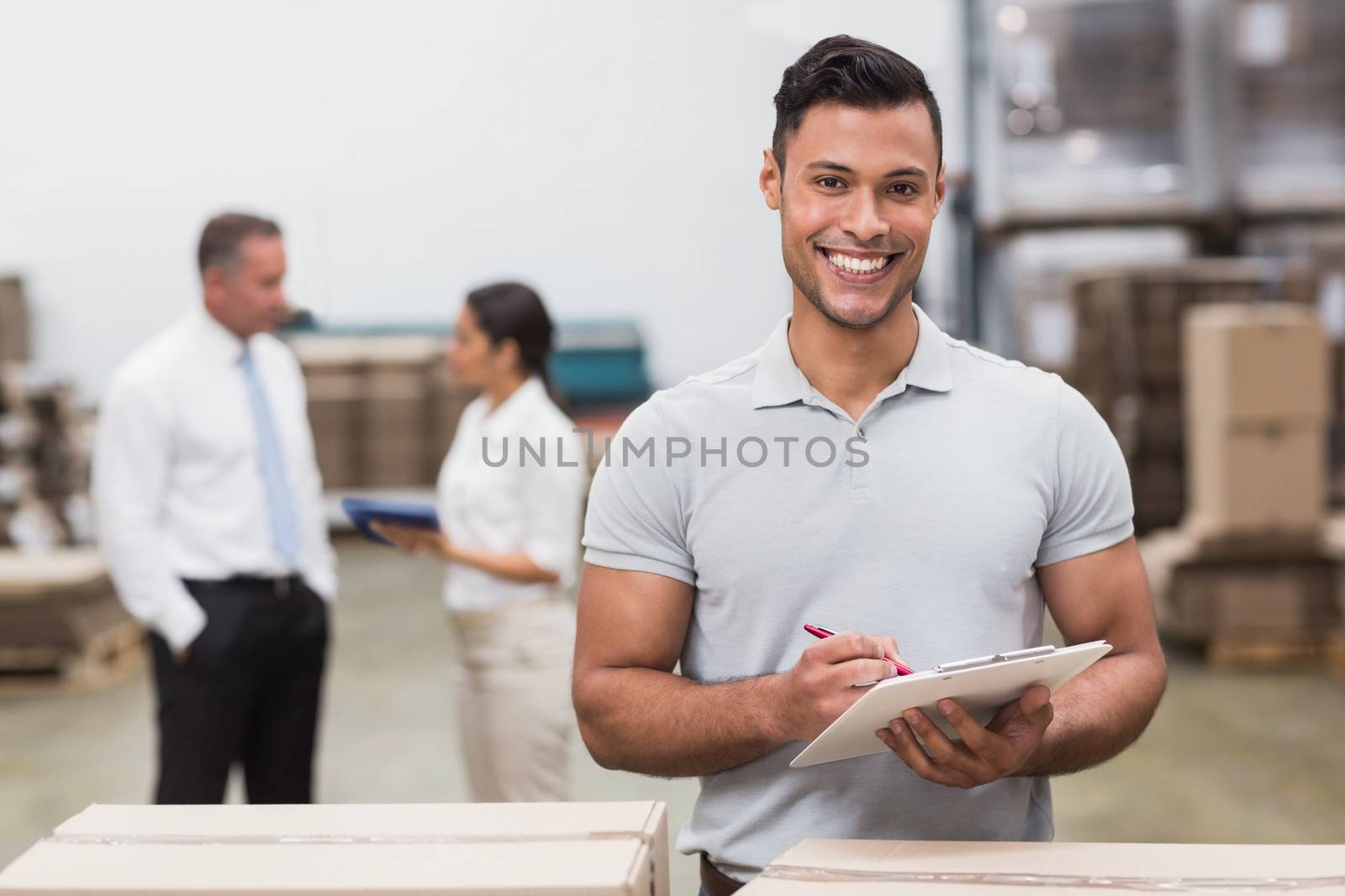 Manager looking at camera while holding clipboard by Wavebreakmedia