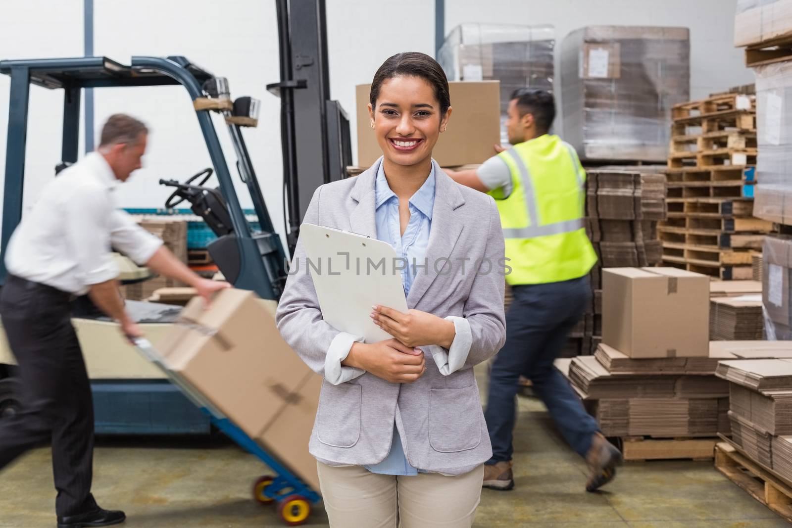 Portrait of smiling female manager holding files during busy period in warehouse