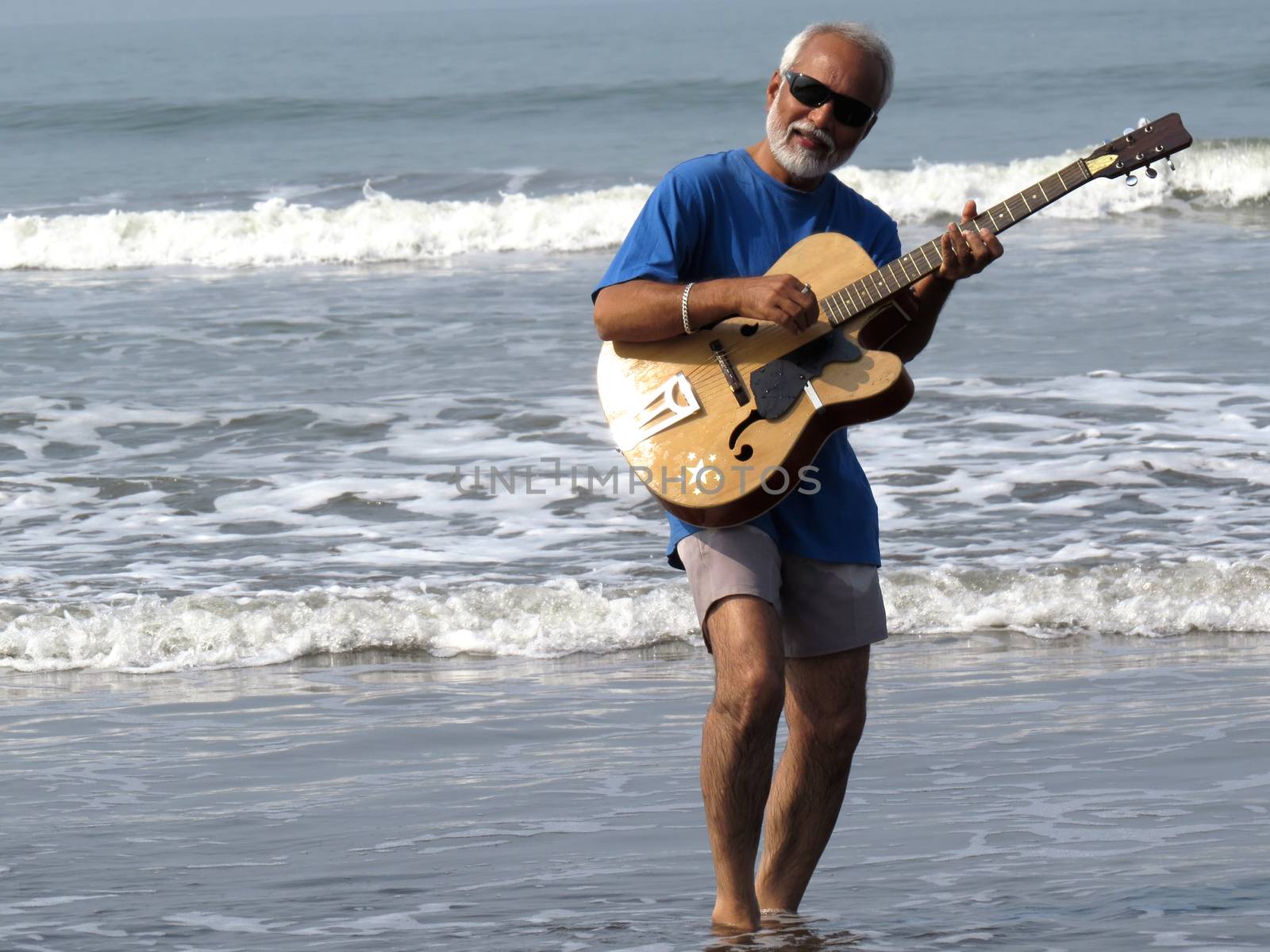 A senior Indian musician playing guitar and singing in the sea                               