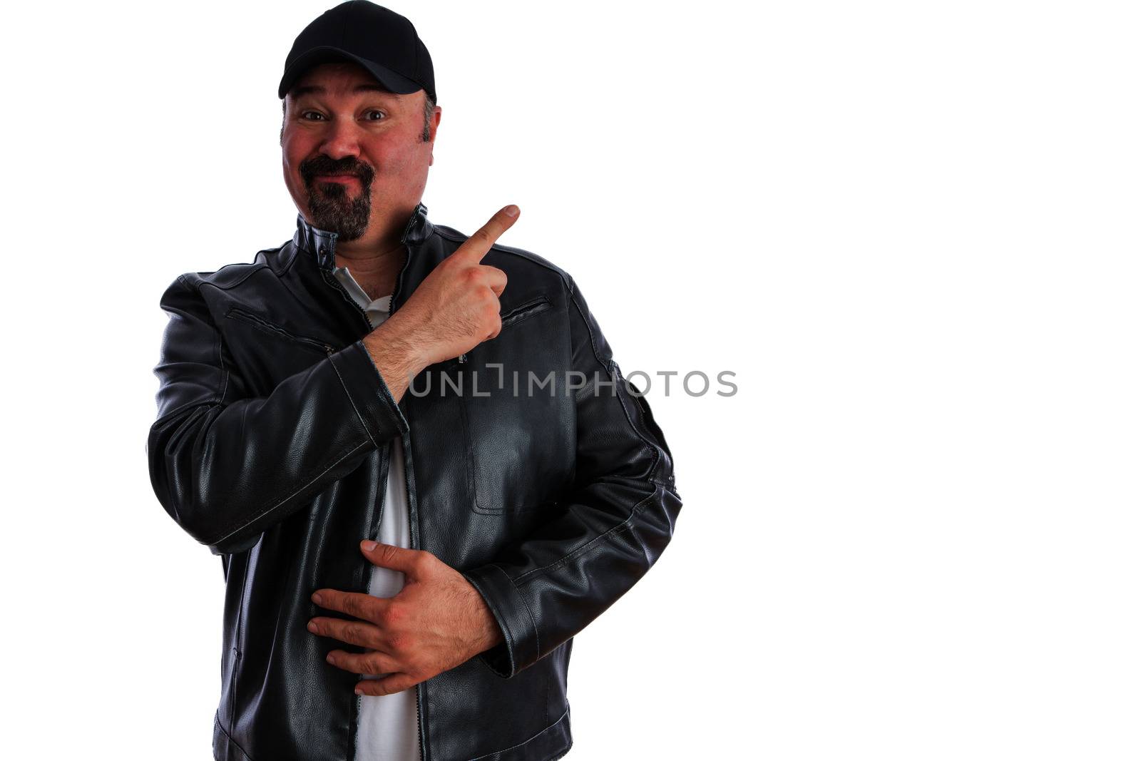 Jaunty trendy middle-aged man with a goatee wearing a grey leather jacket and cap pointing to blank copyspace for your advertising with a pleased expression, isolated on white