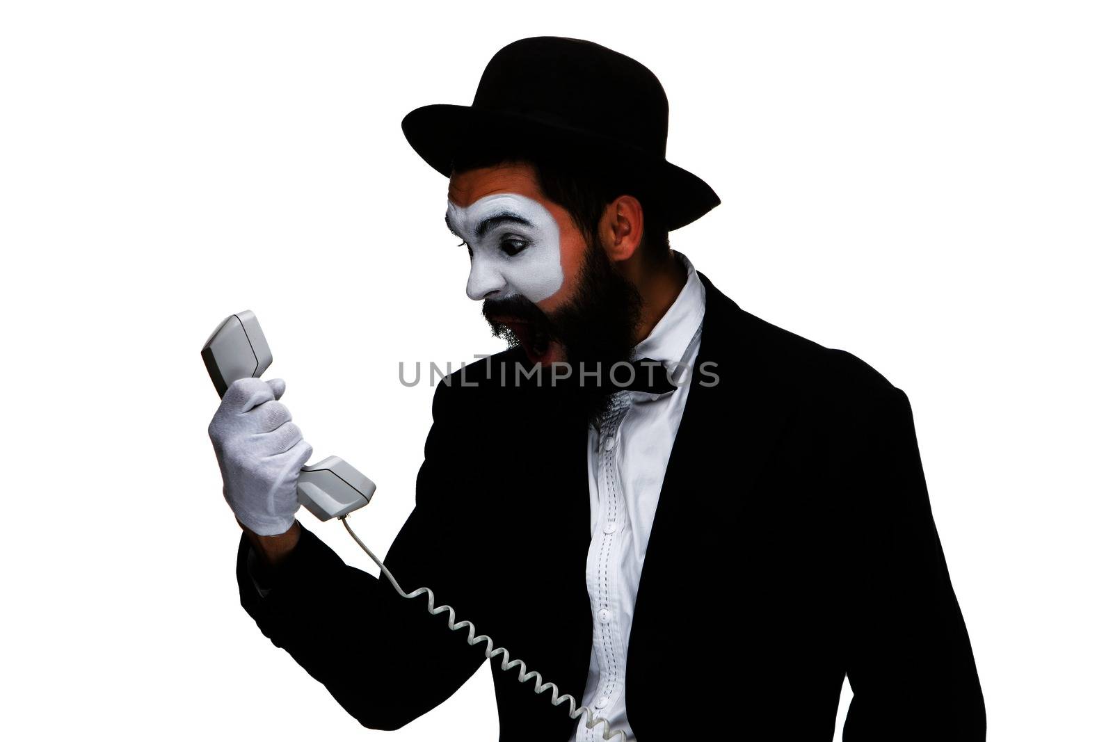An angry and irritated young man screams into the telephone receiver isolated on white background. The concept of business relations