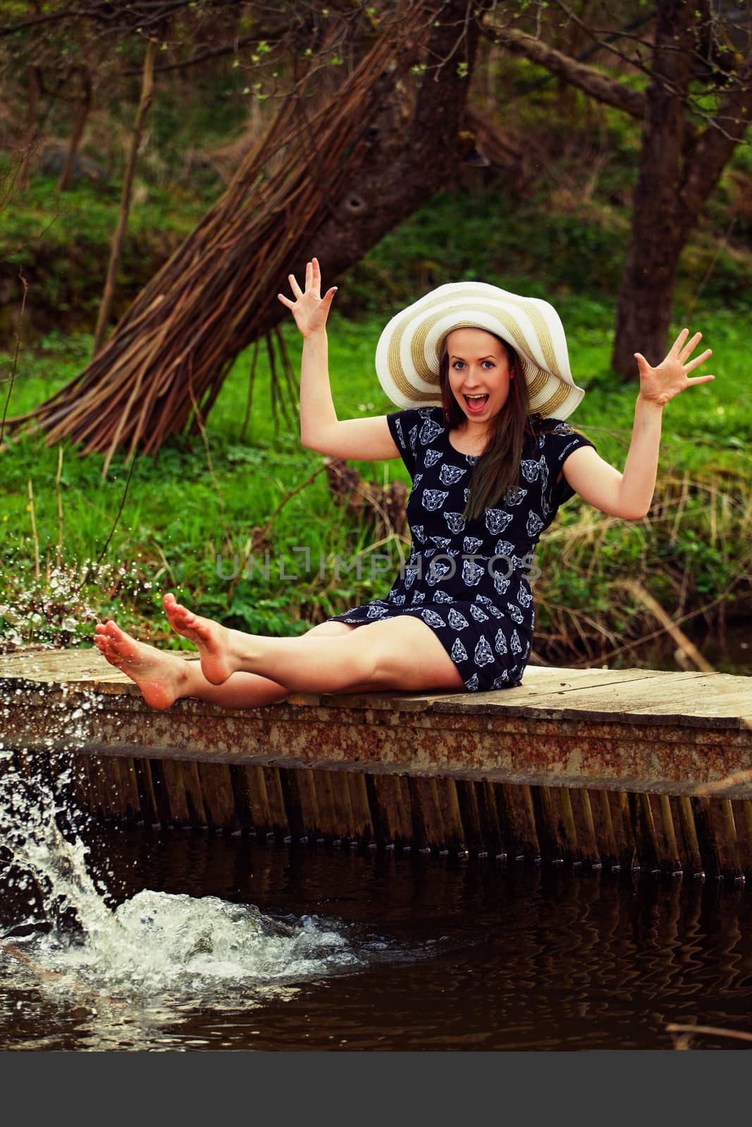 Cheerful fashionable woman sits on small bridge and splashing water by artush