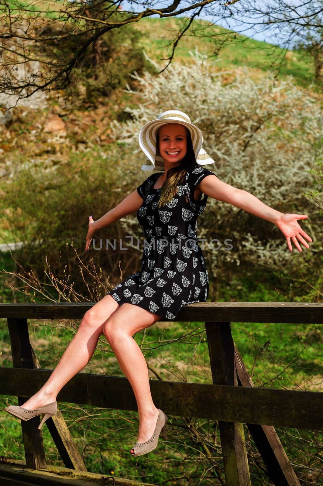 Cheerful fashionable woman in stylish hat and frock posing outdoor. Happy brunette girl with raised hands and smile.