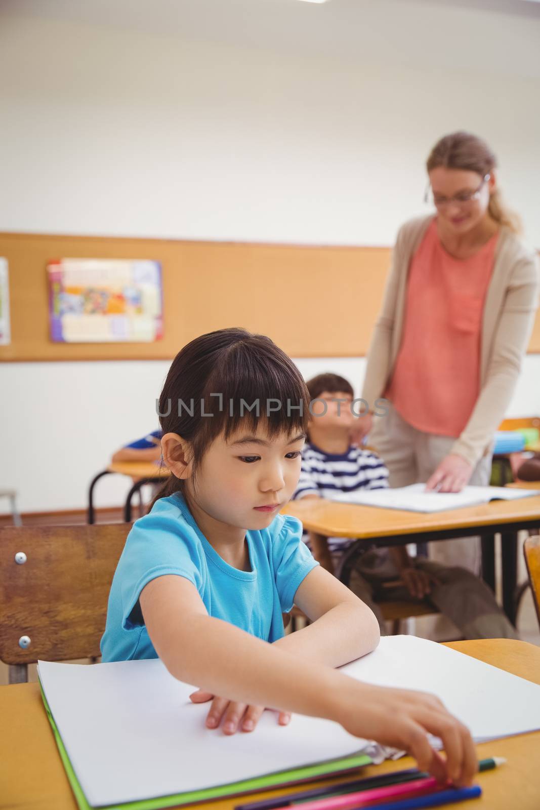Cute pupils writing at desk in classroom by Wavebreakmedia