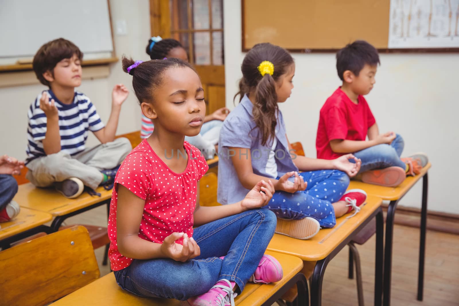 Pupils meditating in lotus position on desk in classroom at the elementary school