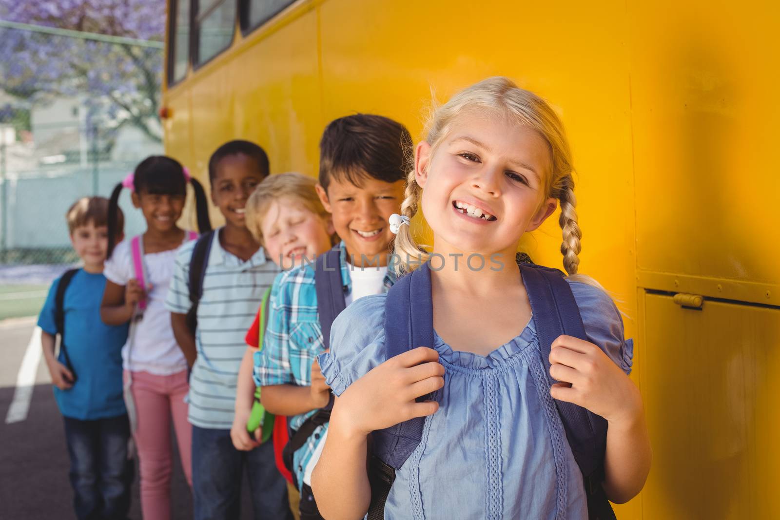 Cute pupils smiling at camera by the school bus outside the elementary school