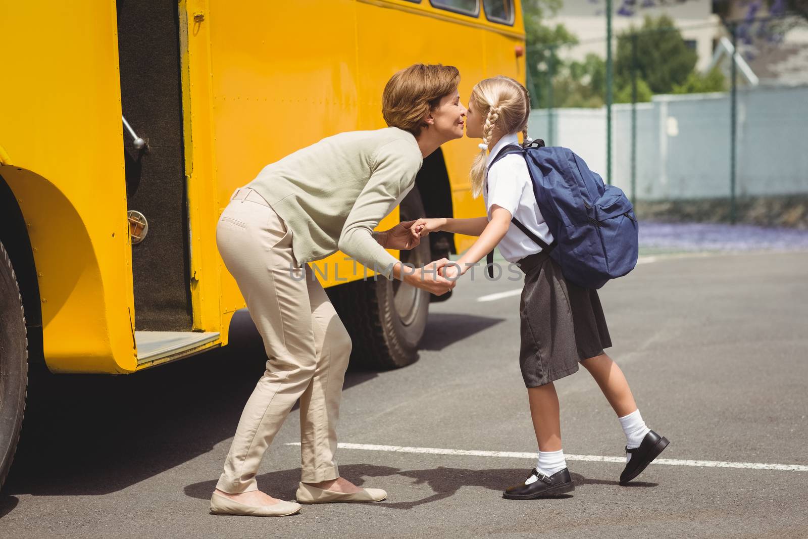 Mother kissing her daughter by school bus outside the elementary school