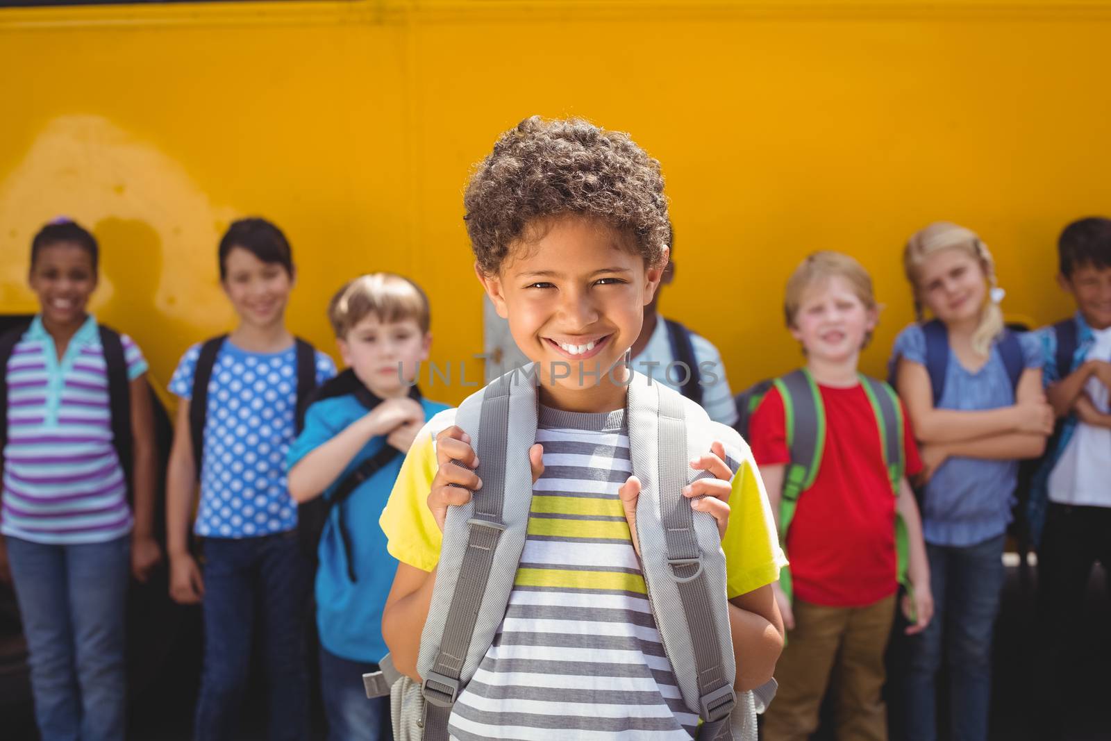 Cute pupils smiling at camera by the school bus outside the elementary school