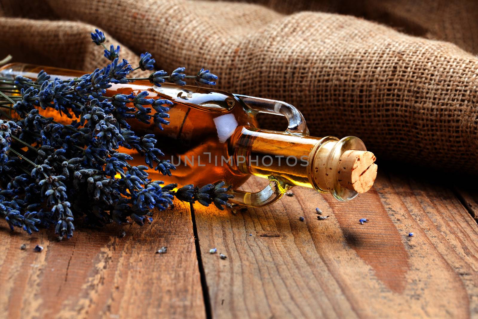 Essential oil botle and lavender flowers, on wooden background.