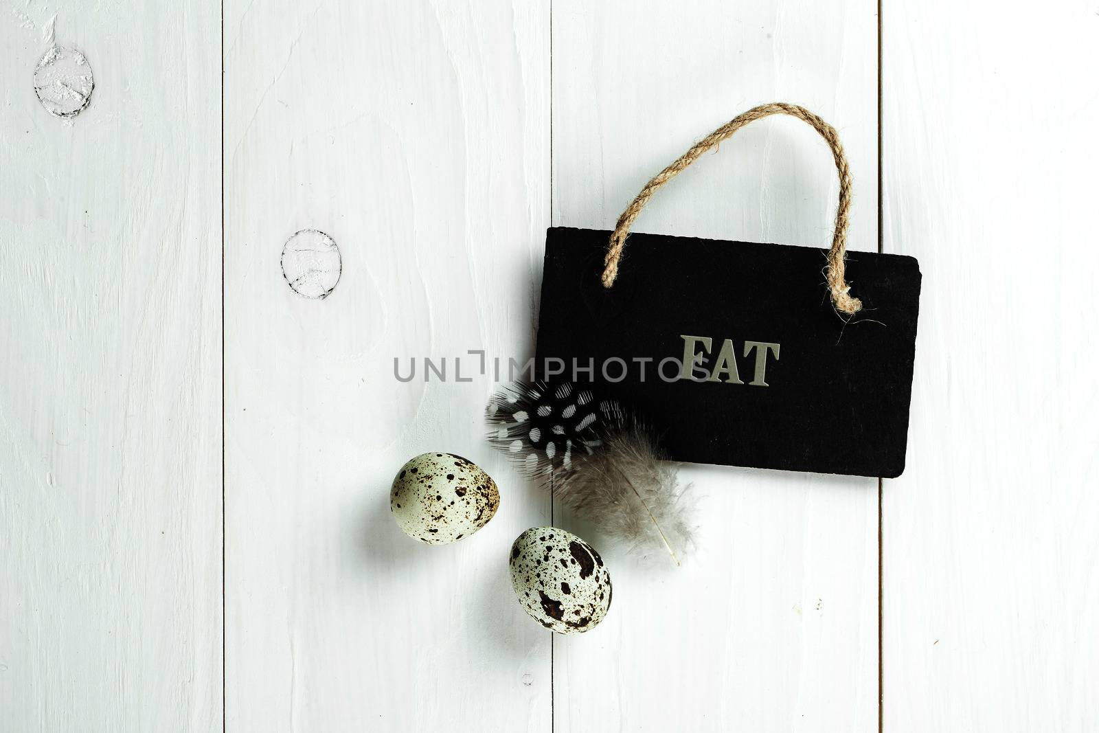 Quail eggs and feather with vintage blackboard on white wooden background, with copy space for greeting text.