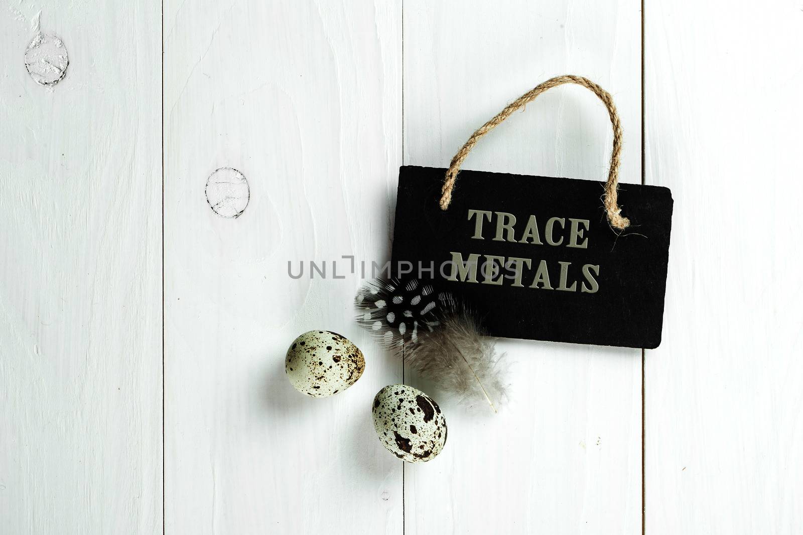 Quail eggs and feather with vintage blackboard on white wooden background, with copy space for greeting text.